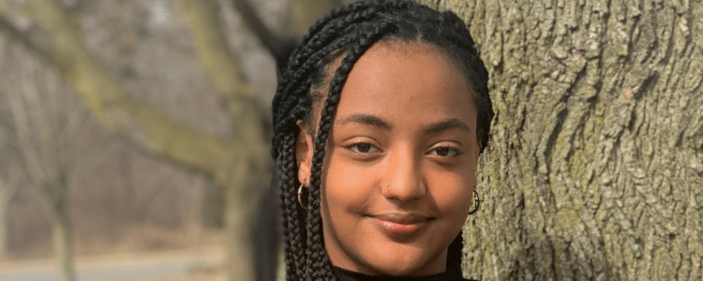 University of Waterloo Arts co-op student, Maya Ghion, in front of a tree and smiling.