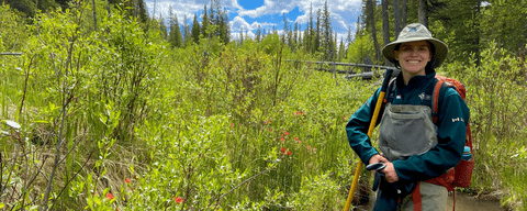 Shelby standing in a creek in overalls and a hat.