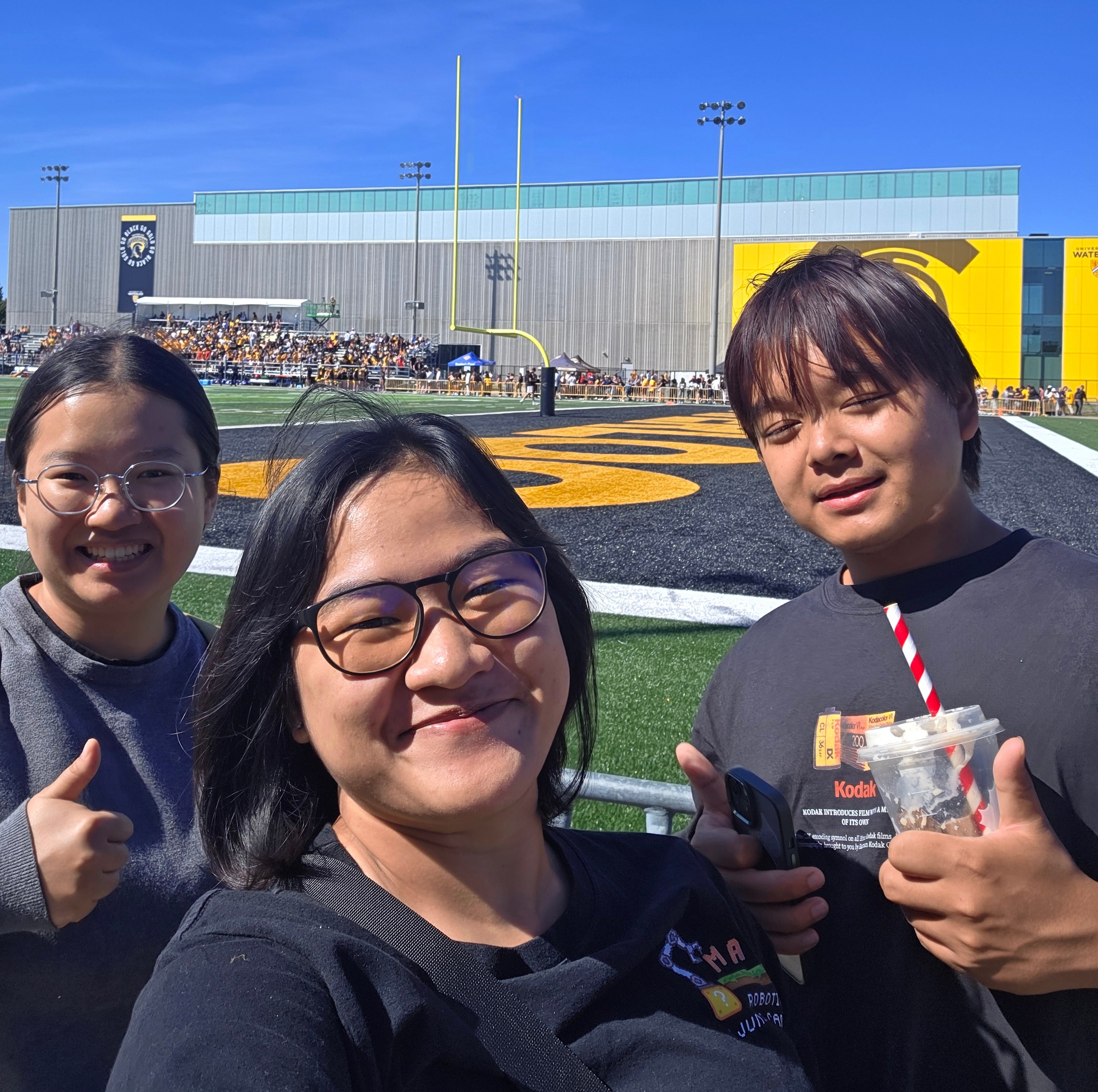Three students standing in front of a football field