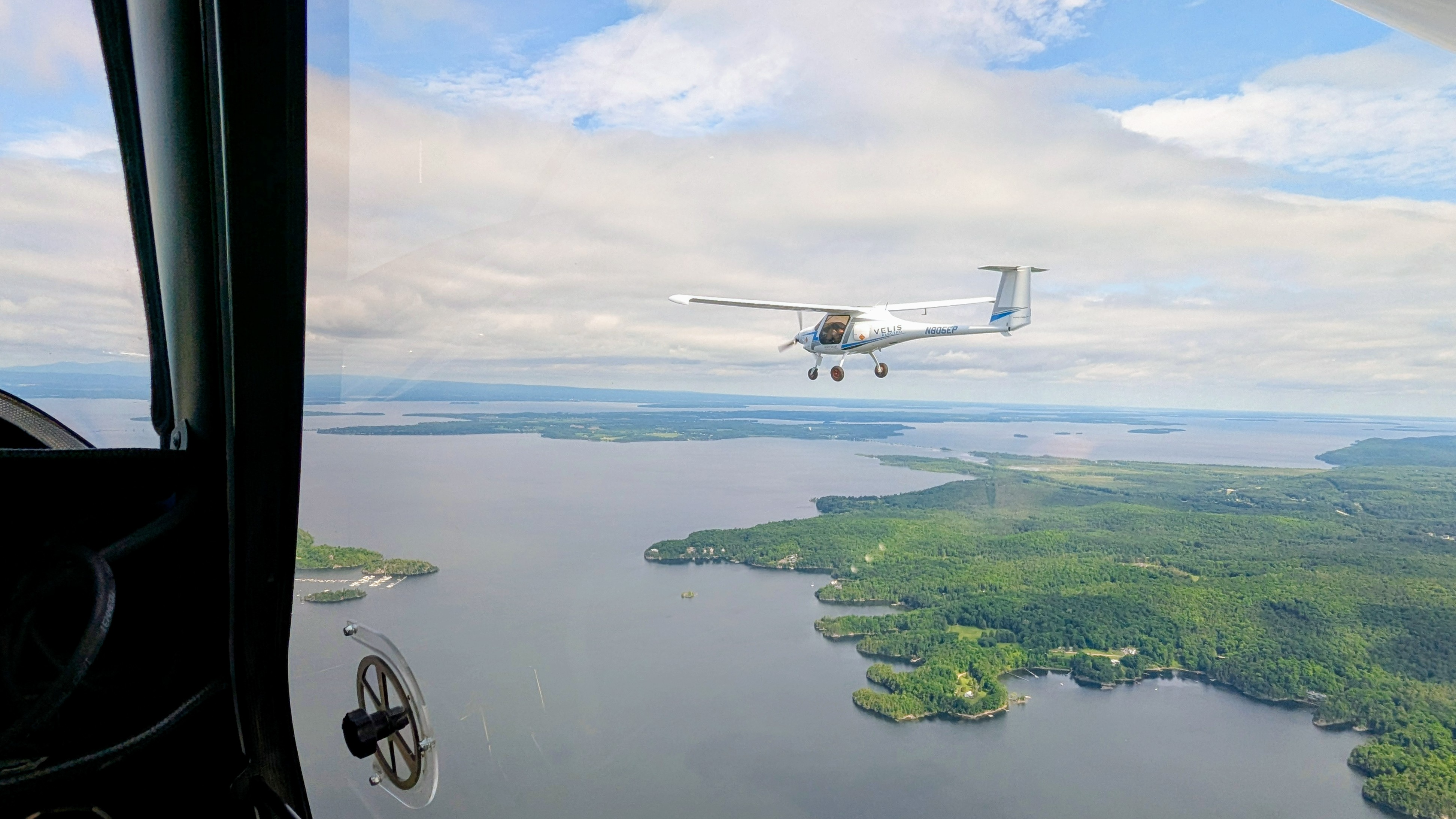 View from an airplane in the sky of another small white plane and the lakes and forest below.