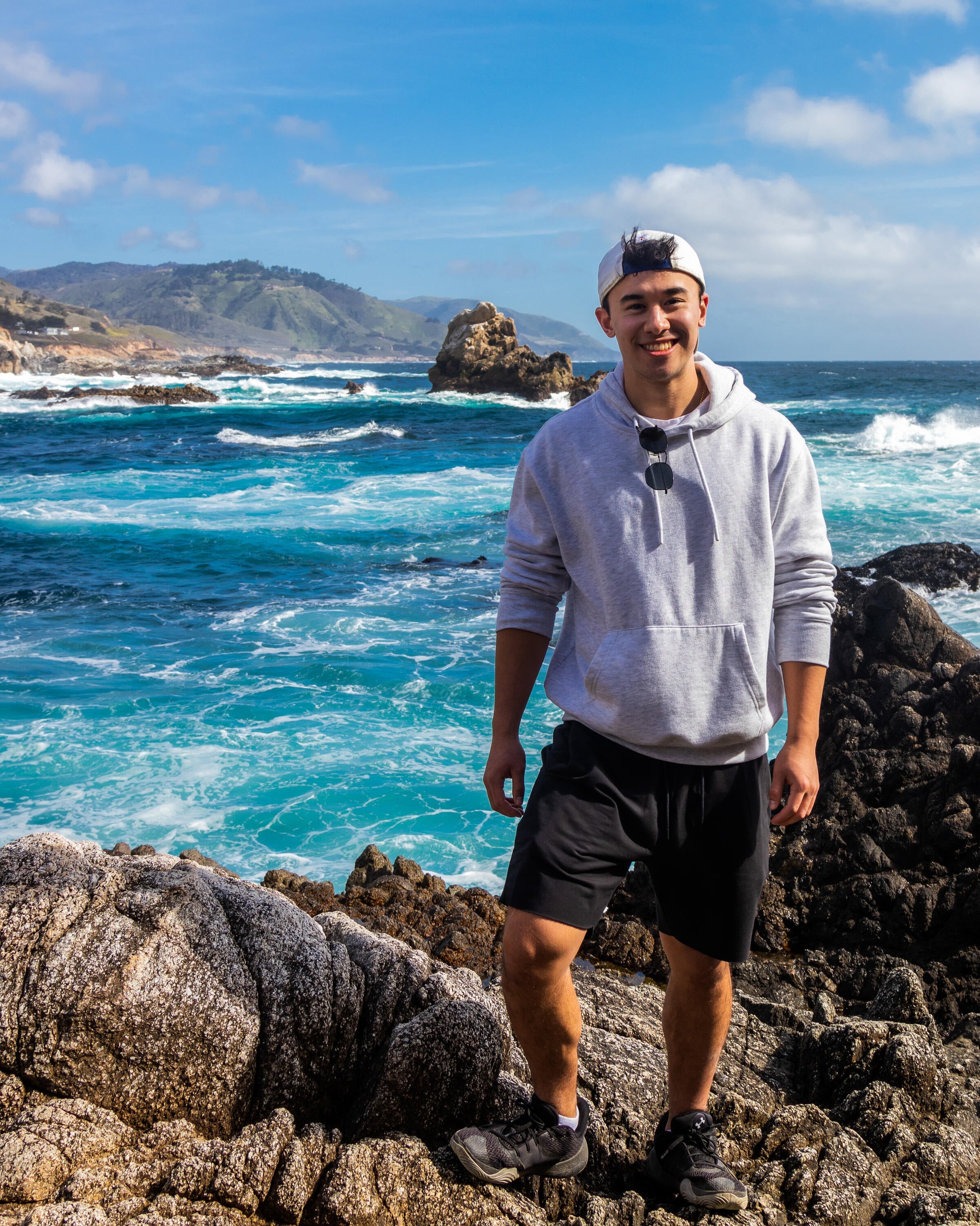 A photo of Brandon standing on rocks by a body of water.