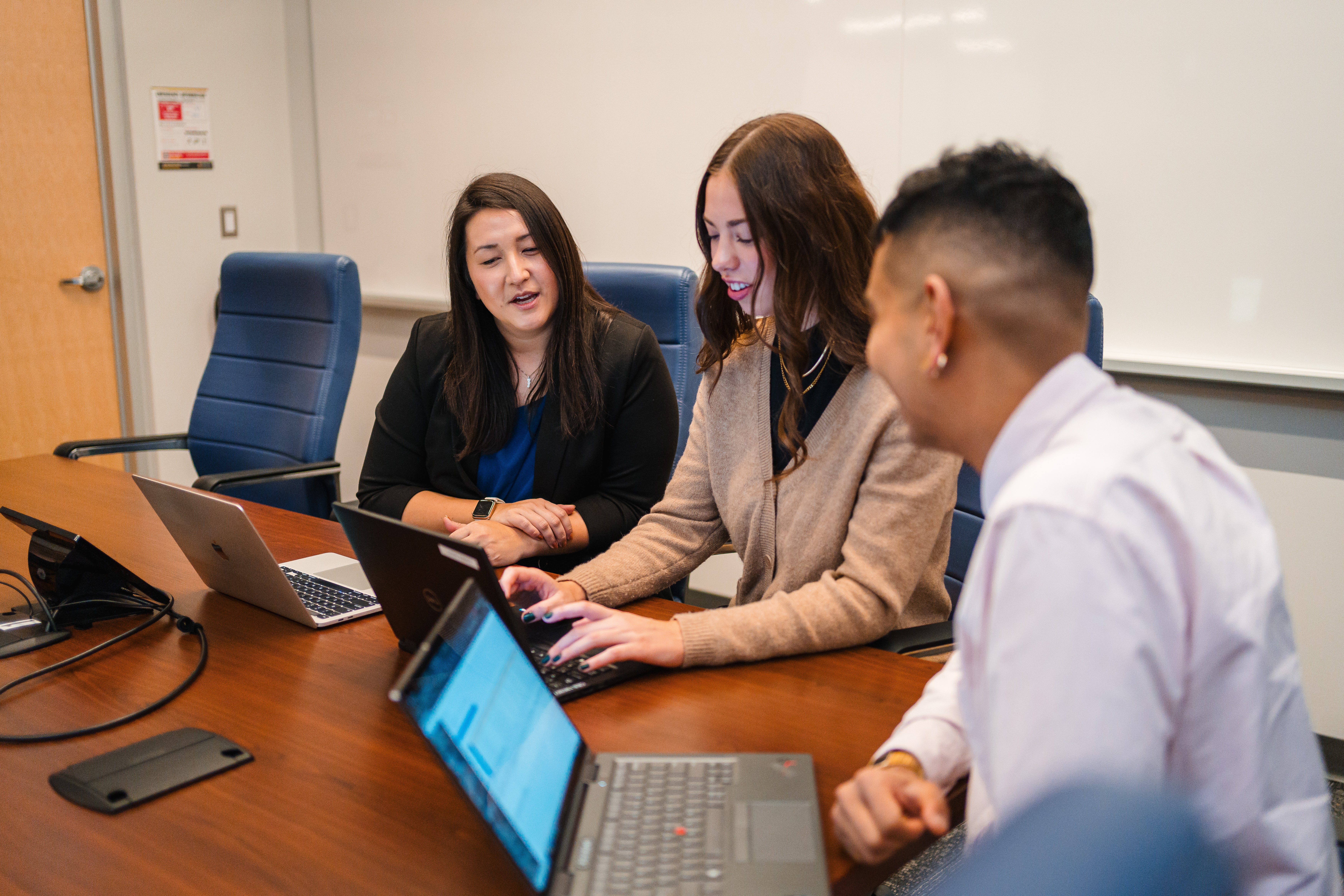 three people sitting at a table looking at a computer screen