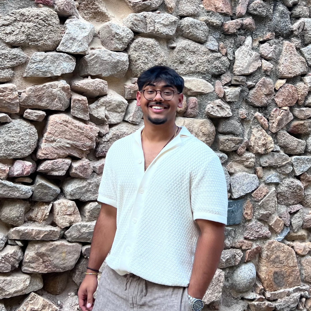 Dev Shah smiling in front of stone wall