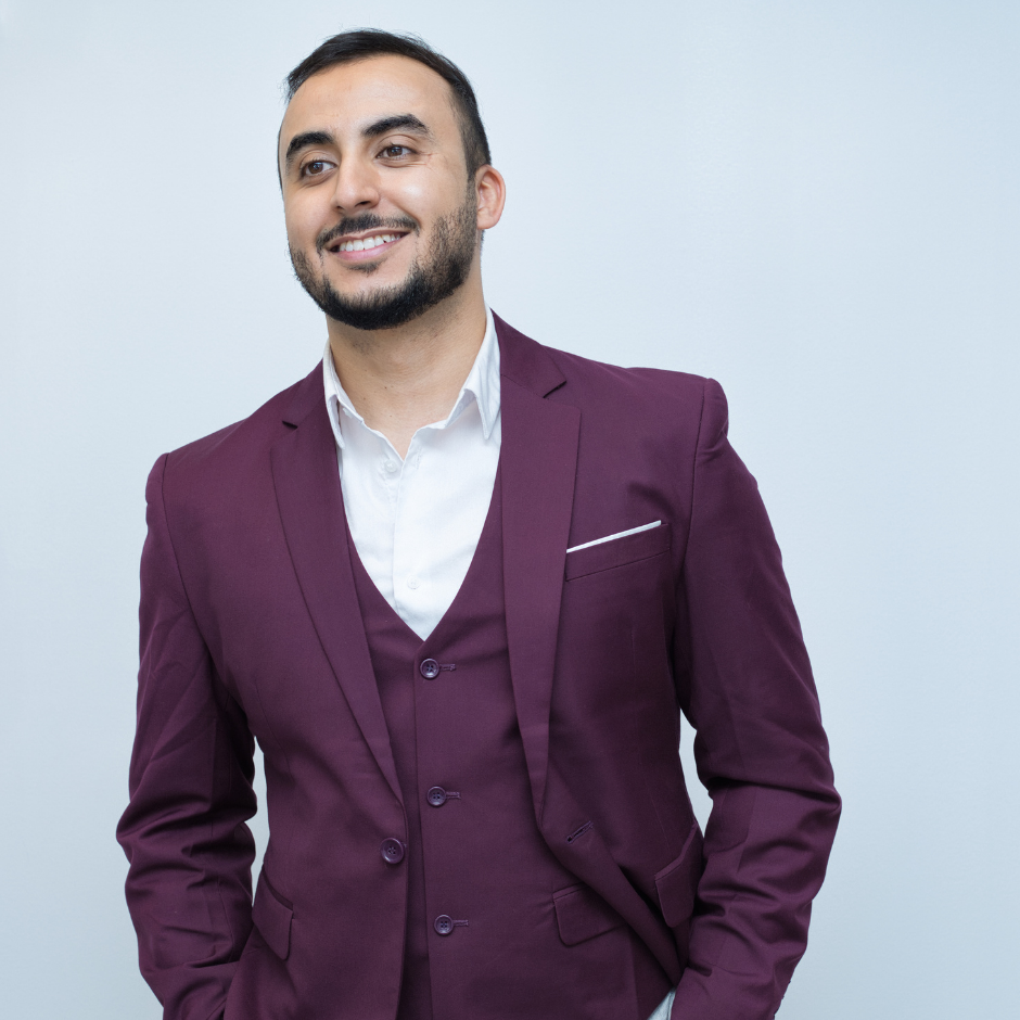 A photo of Abdurrahman in a maroon suit against a grey backdrop.