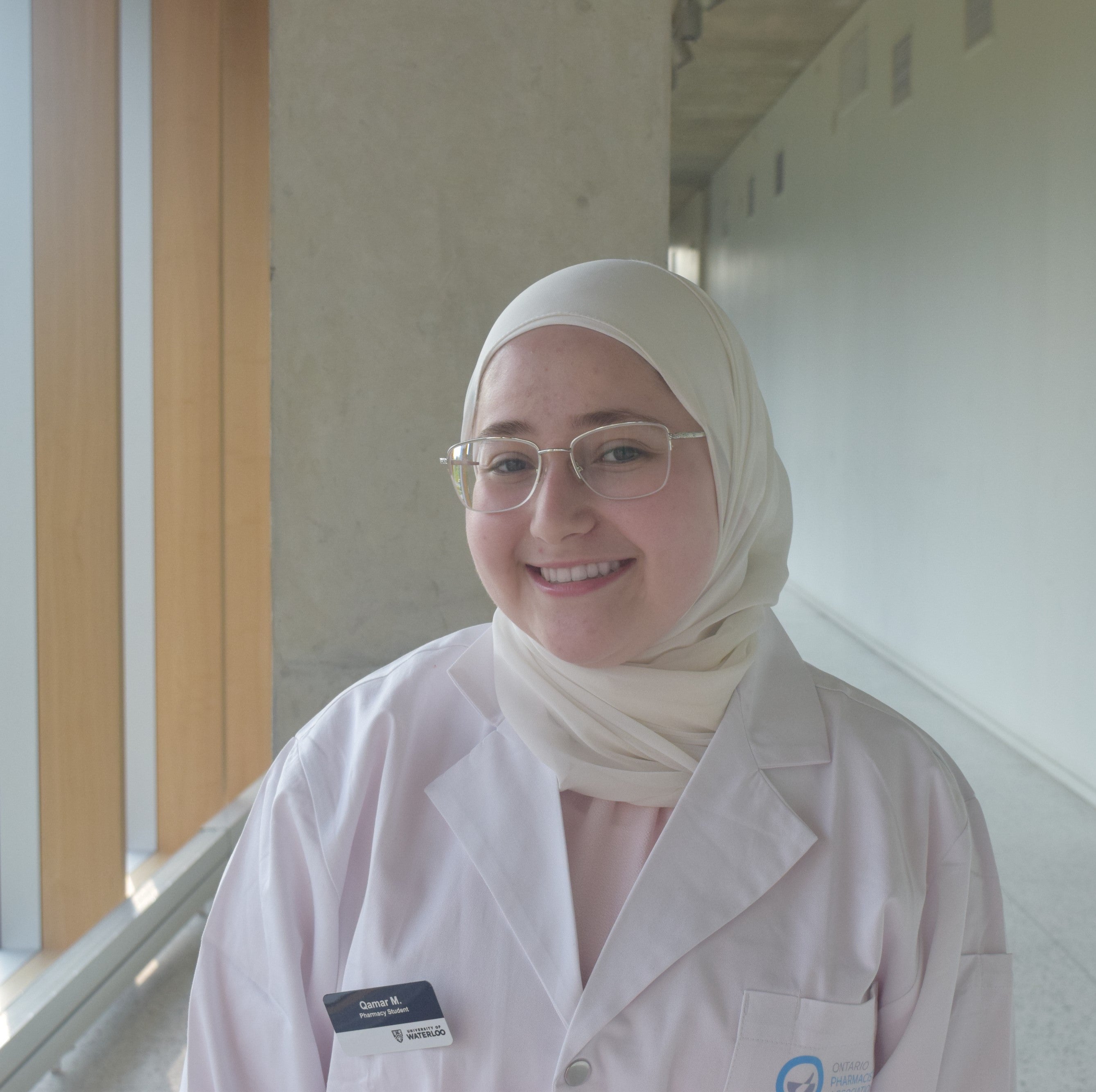 Qamar in a white coat, standing in a hallway.