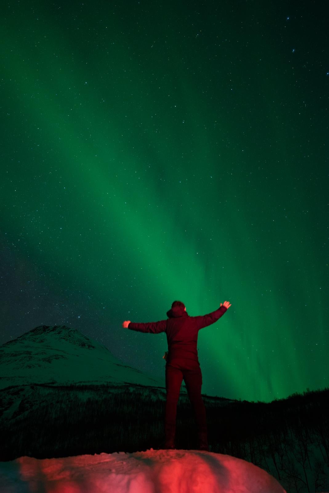 Shawn facing away, with his arms in the air, looking at the aurora borealis.