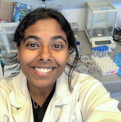 Thenuja Vittanachchi wearing a lab coat, looking up at the camera, smiling.