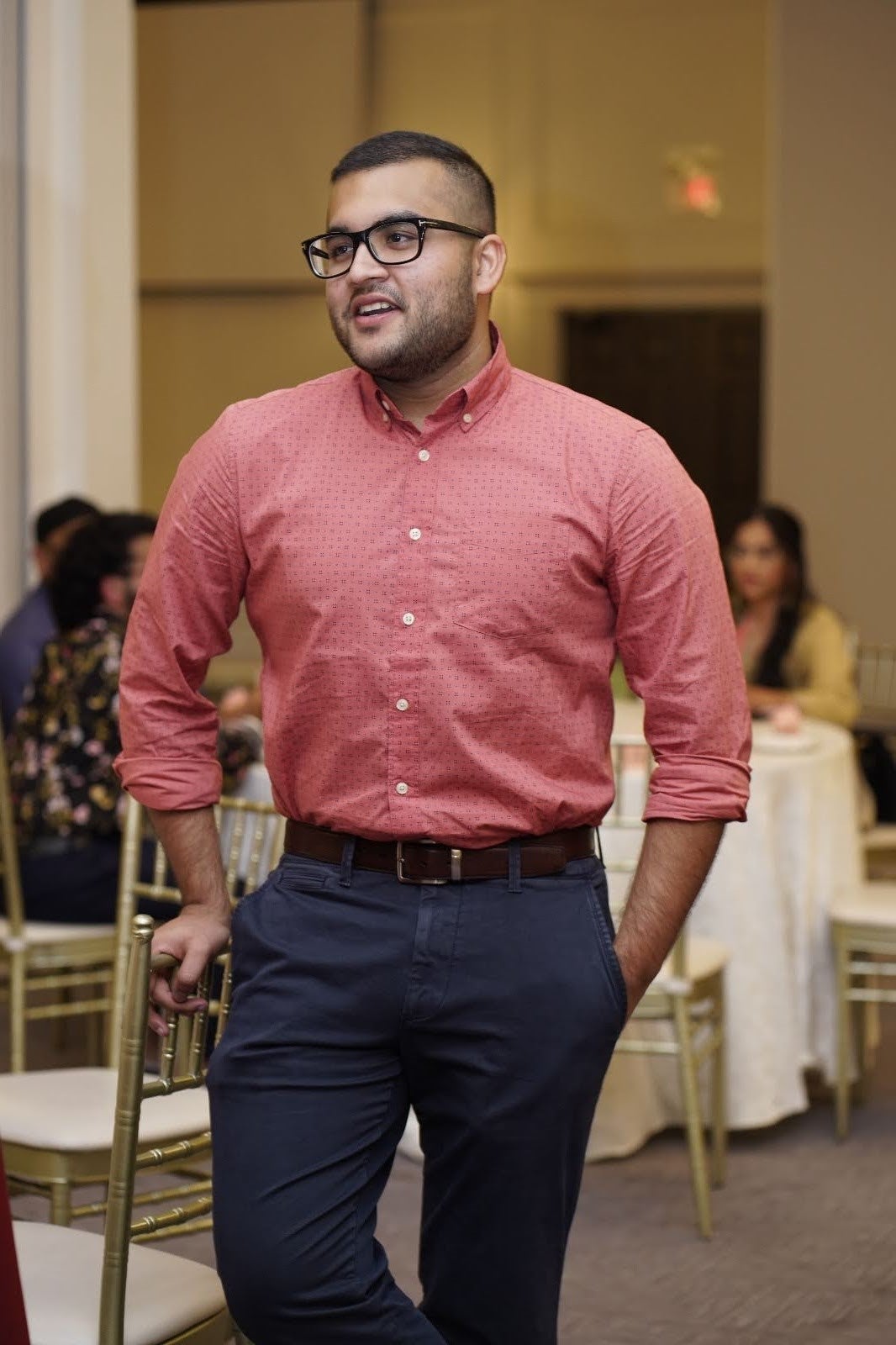 Hussain slightly smiling while standing against a chair in a venue