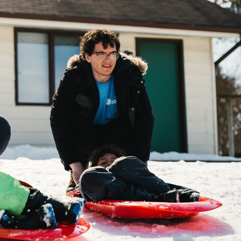 David Orlando pushing a child down a hill for tobogganing