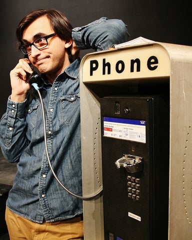 A man leans on an old fashioned telephone booth as he's talking into the receiver