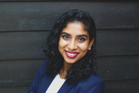 A woman (Smita) smiling.  She is wearing red lipstick, with a dark blue blazer over top of a white shirt.