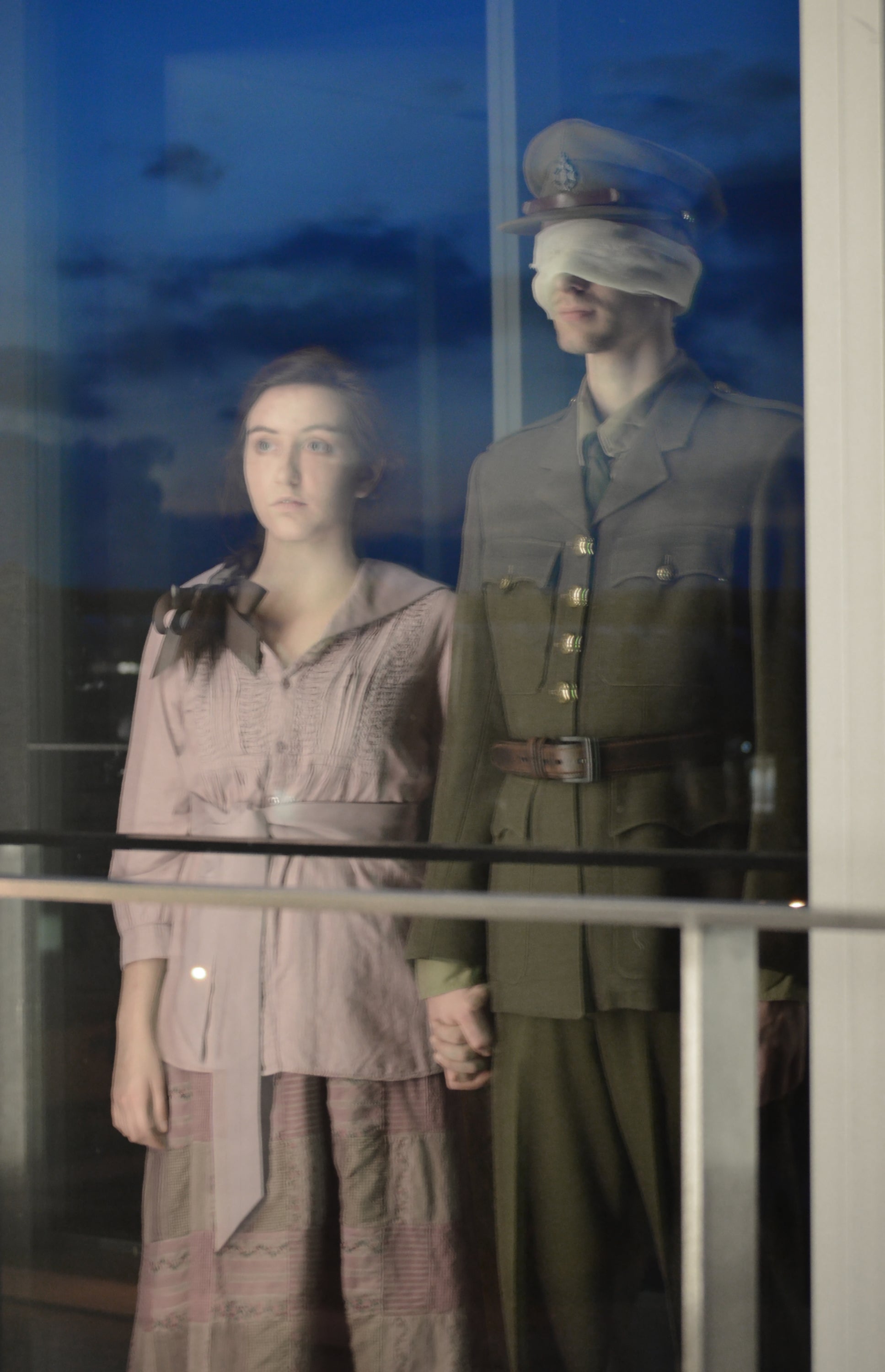 Woman and soldier looking through a window with clouds reflected