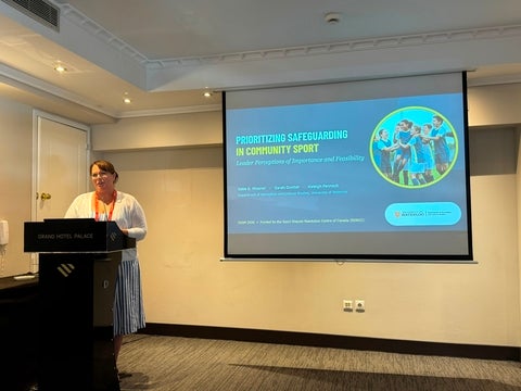 Dr. Katie Misener standing at podium presenting her study titled: Prioritizing Safeguarding in Community sport: leader perceptions of importance and feasibility