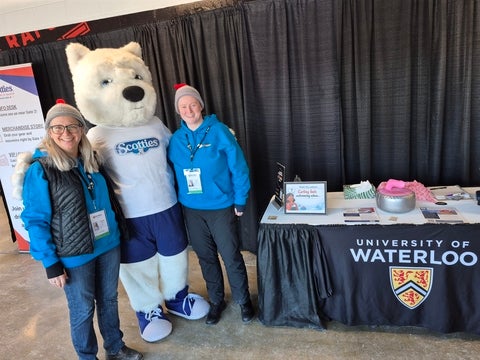 Dr. Heather Mair and laura Leitch pose with the Scotties mascot in front of their information booth