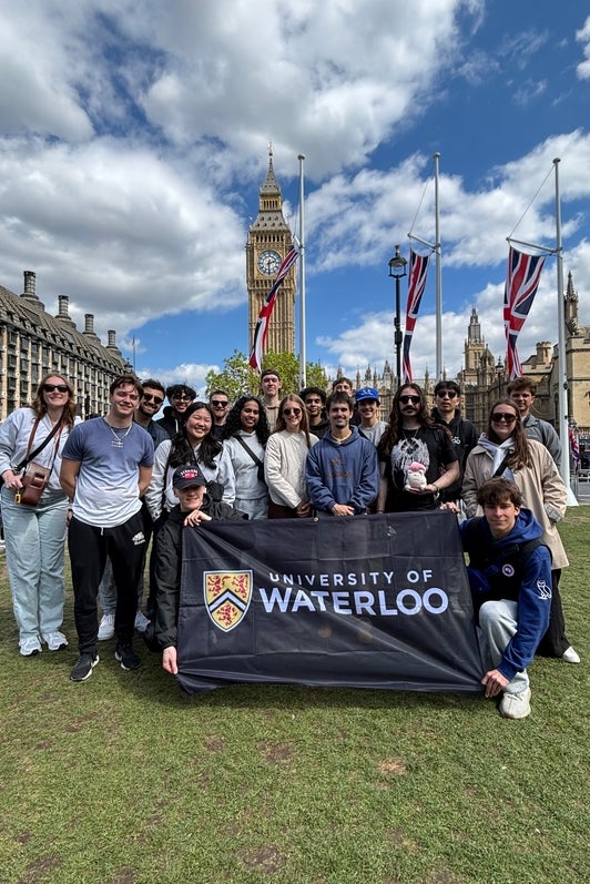 A group of students gathered in front of the Big Ben Tower holding up a University of Waterloo Flag