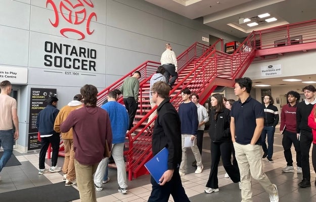Event staff and volunteers wearing red shirts pose together along the rink boards at a hockey arena, smiling for a group photo during a tournament.