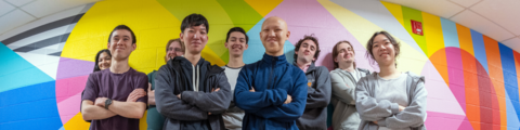 9 students standing against a colourful wall