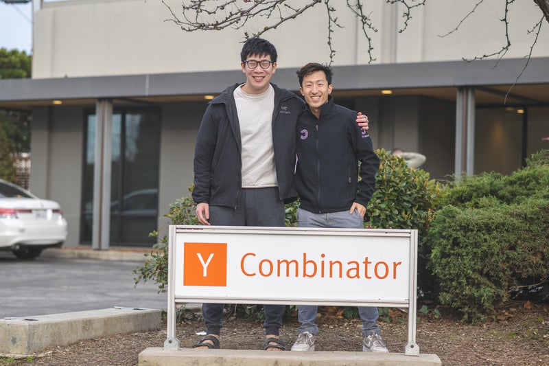 Jeff An and his co-founder posing in front of the Y Combinator sign outside YC's office