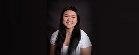 An Asian woman in a white t-shirt posed in a black background (similar to those photo studio backgrounds)
