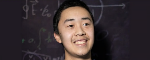 An Asian man smiling in front of a blackboard with math equations