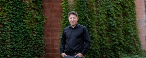 Banner of Nathan Hoel aganist a red brick wall with vines hanging down