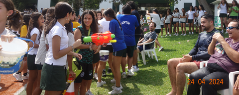 a bunch of school kids holding water guns and water buckets to pour water on their teachers sitting down on lawn chairs