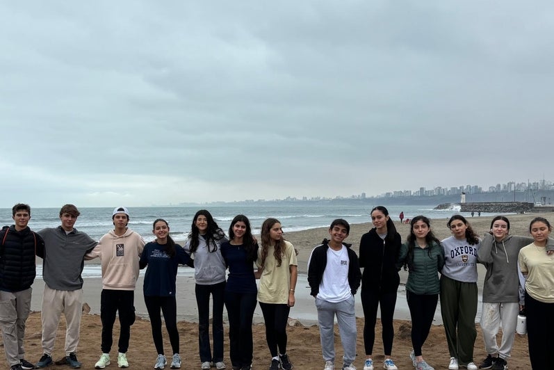 A group of people (wearing hoodies and long sleeve shirts) standing side-by-side on a beach. In front of them are trash bags 