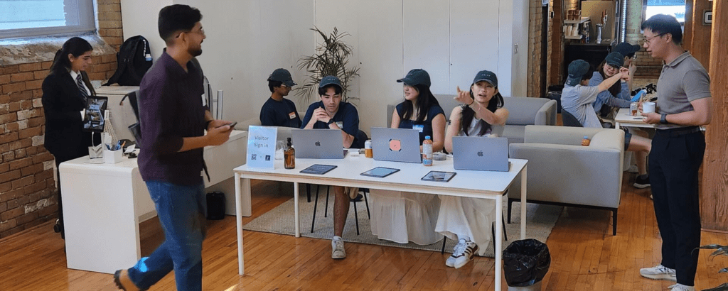 A group of people at a table with laptops and drinks in a casual office space, while another person walks by.