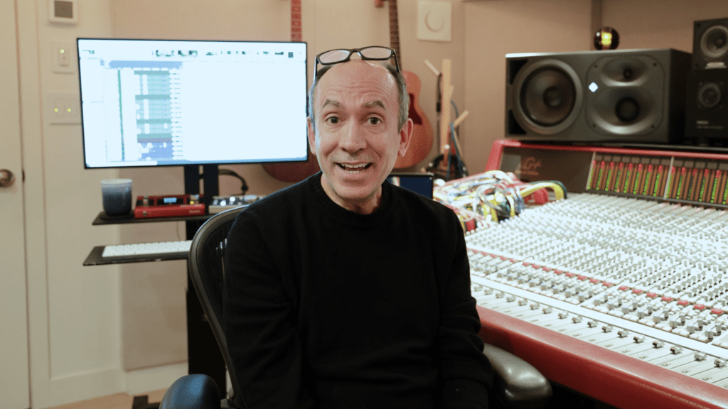 A Portuguese man wearing a long-sleeve black shirt and glasses on his forehead posing in front of a music soundboard/keyboard