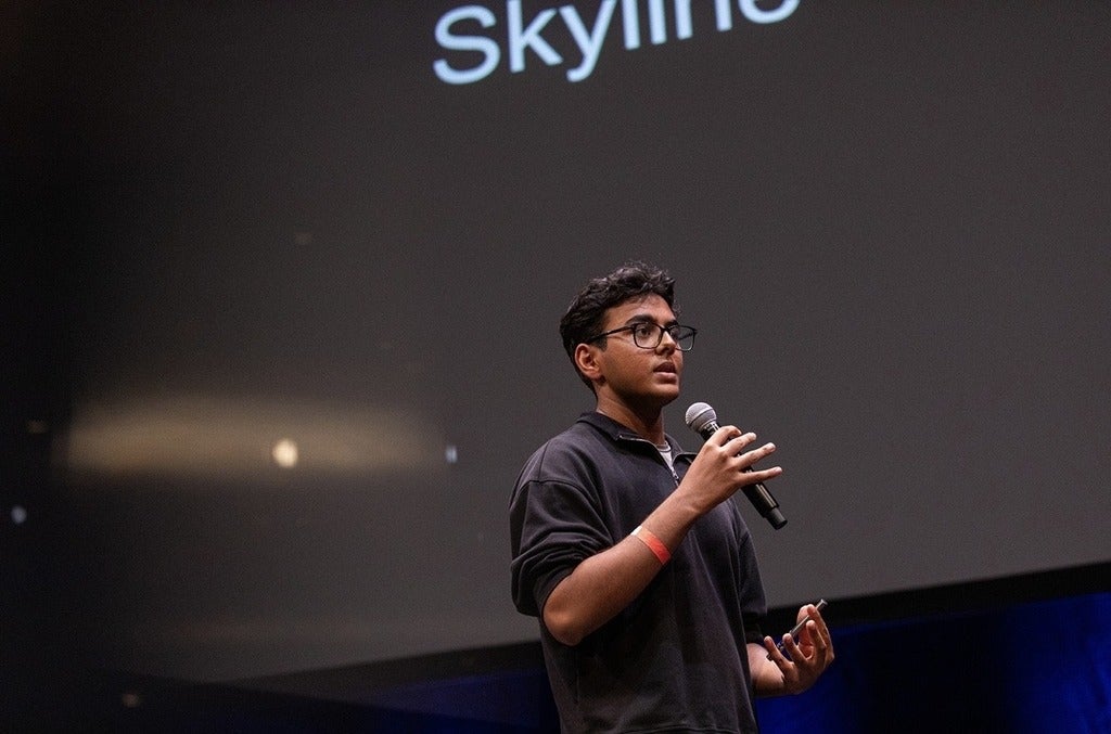 Student holding a mic and presenting skyline. Backkground is a black colour slide, with "skyline" in white text 