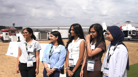 all-female team wearing business clothing. background are a bunch of fire trucks and airplanes.