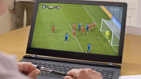 Someone using a laptop to watch a soccer match. The team is huddled near the net. You can see the viewer's hand view on the laptoo but not their face