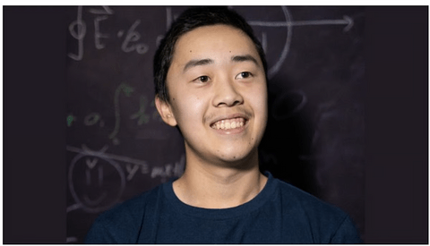 An Asian man smiling in front of a blackboard with math equations