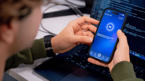 Close-up of someone holding a phone. The screen is blue and it reads "Hey good to have you back. How much time do you have for us today?""