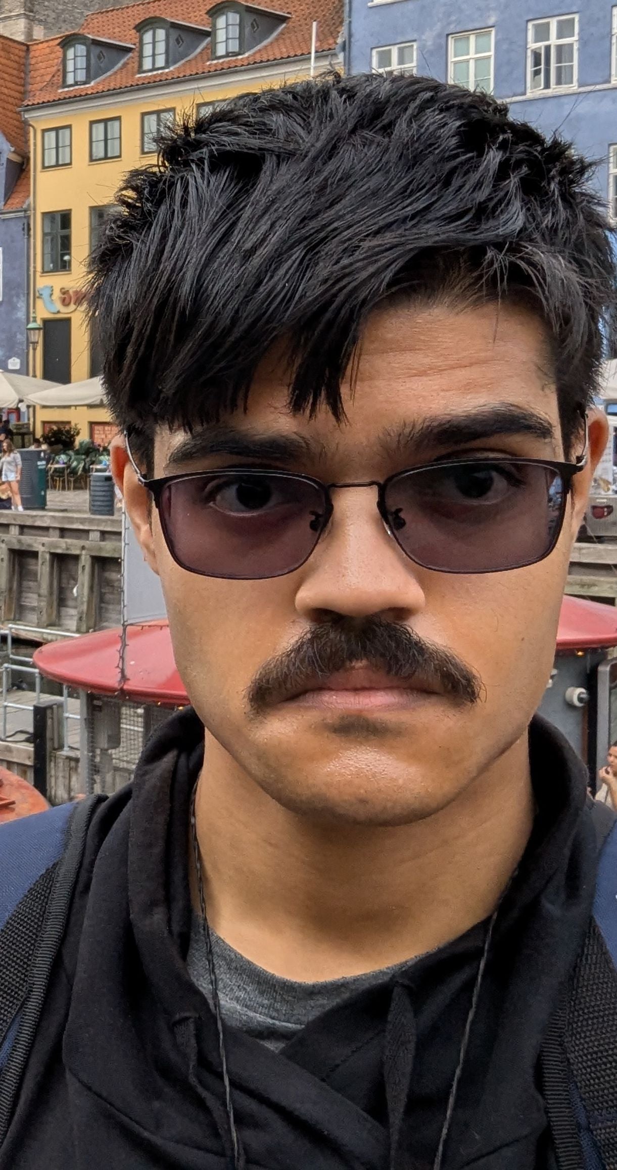 South Asian male donning sunglasses standing in front of colourful houses