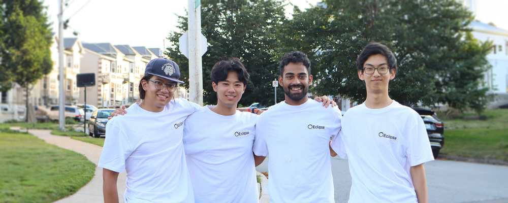 Group shot of Eclipse co-founders, donning their Eclipse merch (white shirts with company logo) and standing in a suburb area