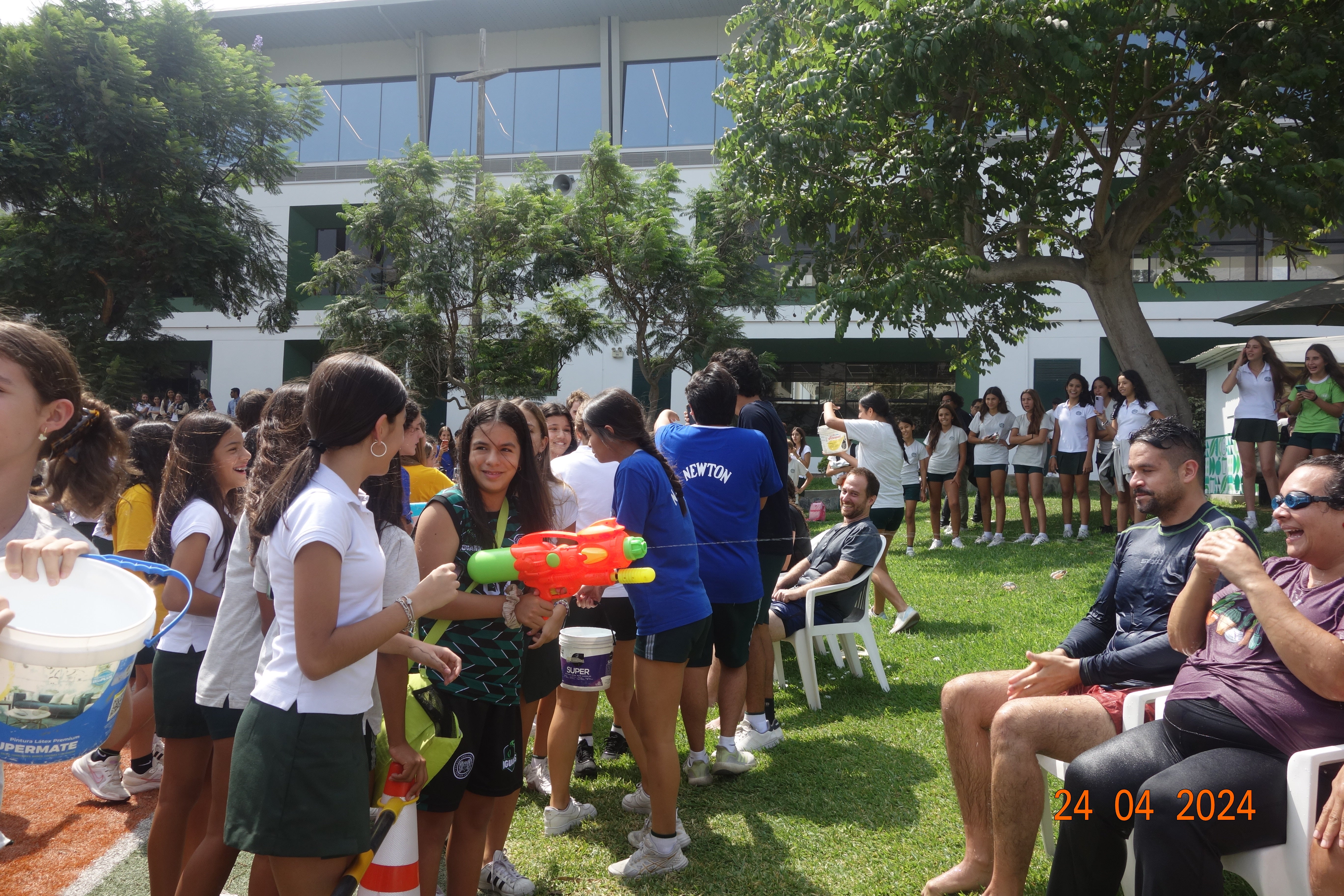 a bunch of school kids holding water guns and water buckets to pour water on their teachers sitting down on lawn chairs