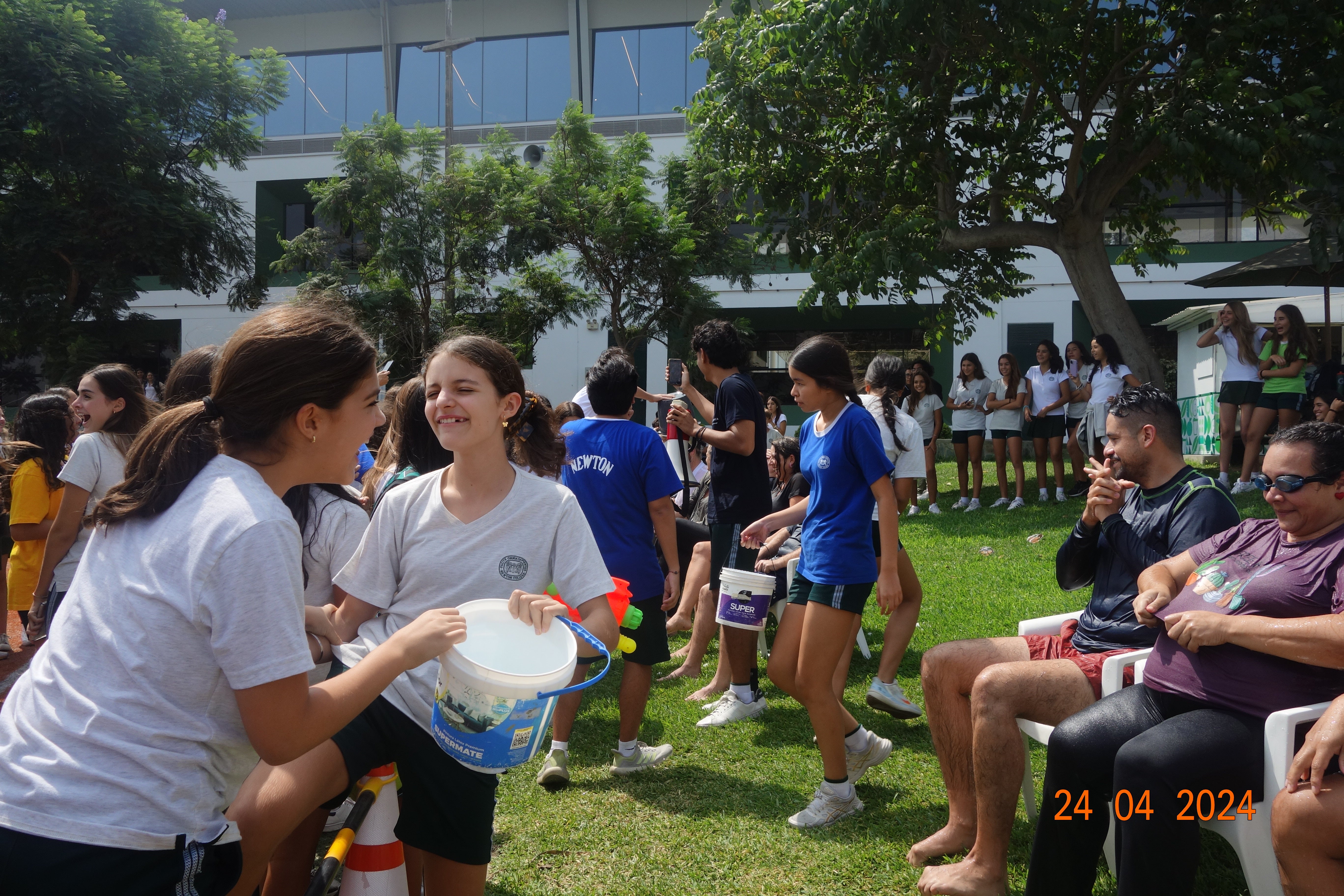 a bunch of school kids holding water guns and water buckets to pour water on their teachers sitting down on lawn chairs