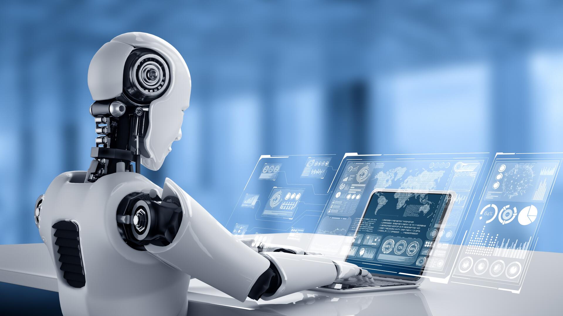 A humanoid robot is seated at a desk, interacting with a laptop. The screen displays futuristic holographic data and graphics, including charts and maps, in a high-tech environment.