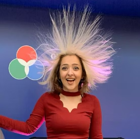 a Middle Eastern woman wearing a red-shirt at the Ontario Science Fair. Her hair is flying up because of the static science exhibit