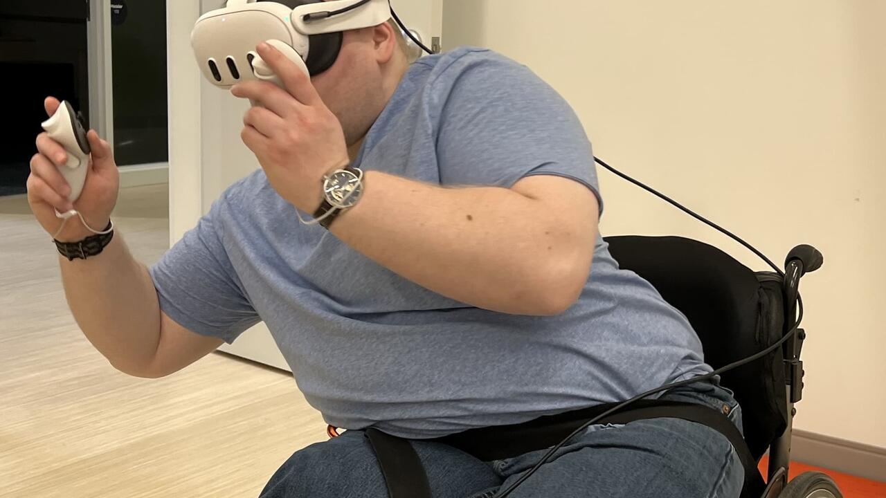 someone in a wheelchair leaning sideways while playing a VR game (wearing vr headsets and holding vr sticks)