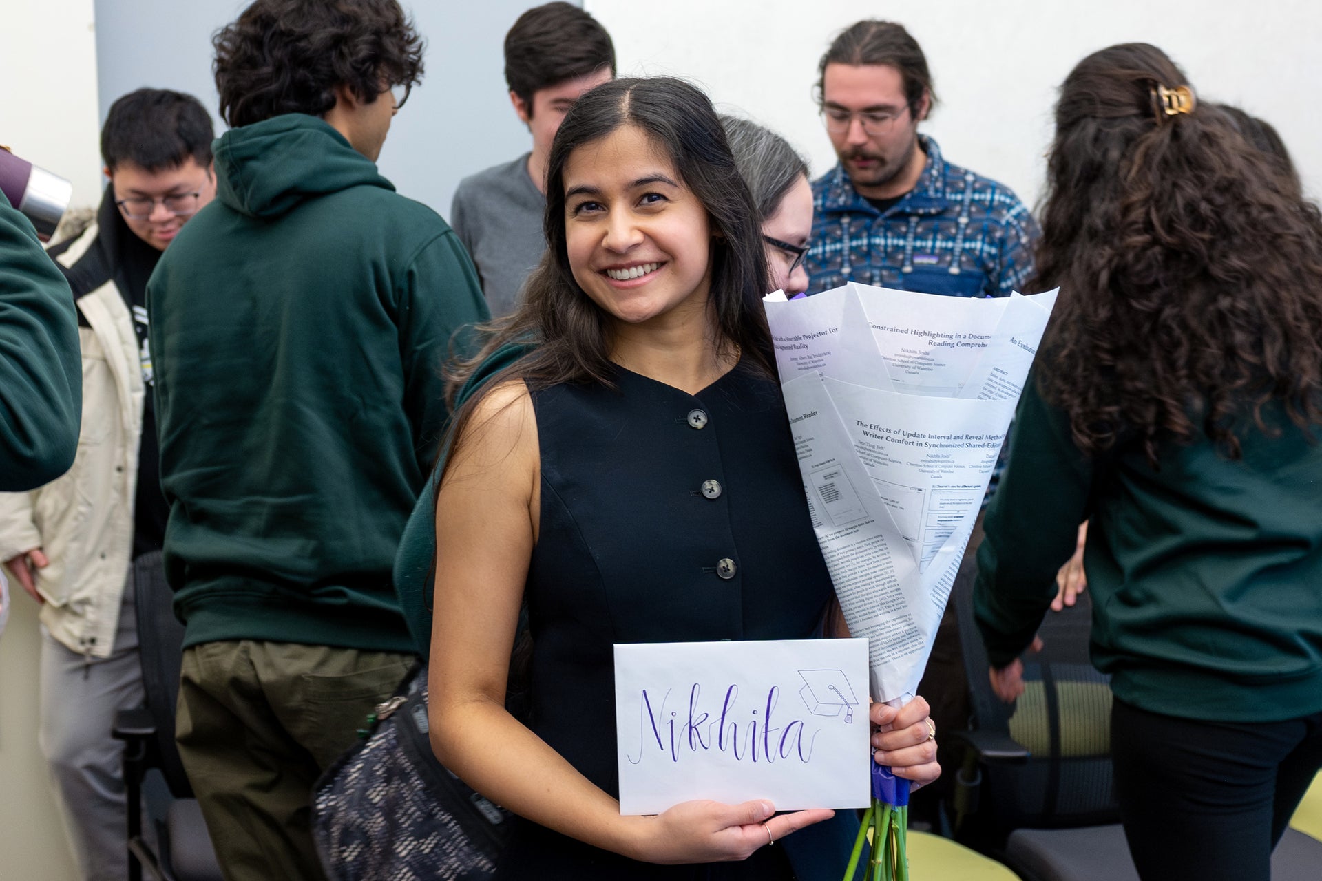 Nikhita donning a navy-blue dressing holding a bouquet (which is composed of her research papers) and an envelope that says "Nikhita"