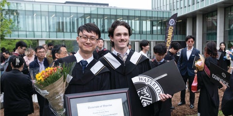 Two students graduating in gowns and holding their degrees