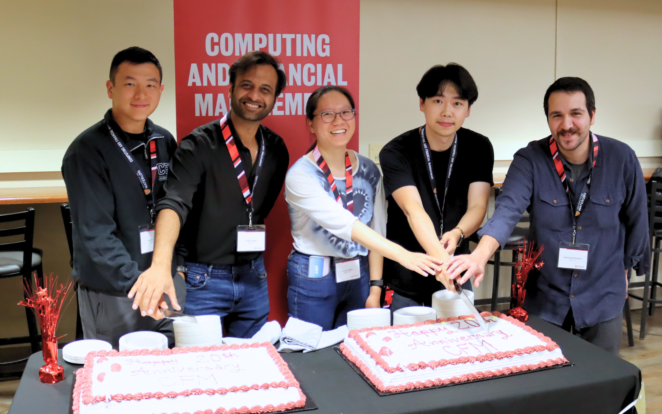 Five alumni cutting cake with a knife