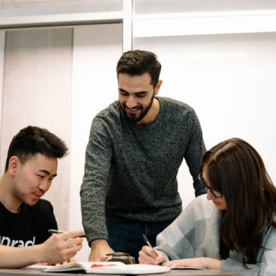 Esteban Veintimilla talking to two students and leaning over desk