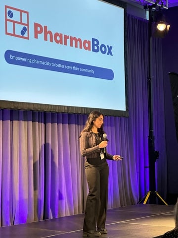 Student standing on a stage with "Pharmabox" written on screen behind.