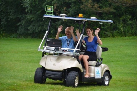 Wayne and Lindsay in a golf cart with their hands up