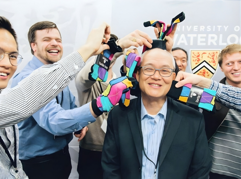 Professor Wayne Chang seen smiling as laughing students surround him with socks.