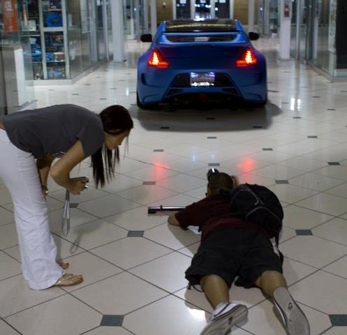 Rachel and a cameraman behind a car driving inside a mall