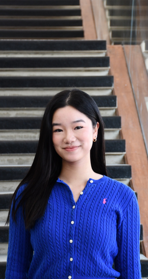 Hayley So smiling in front of stairs wearing blue cardigan with long black hair